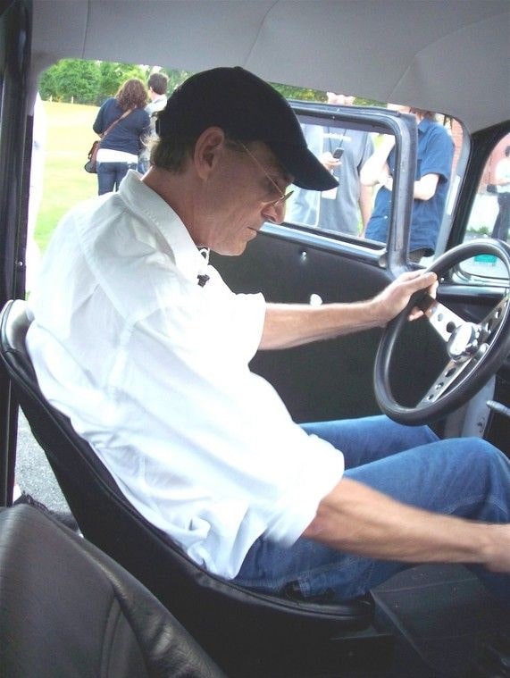 James Taylor in his vintage car while holding black steering in his white shirt and blue jeans